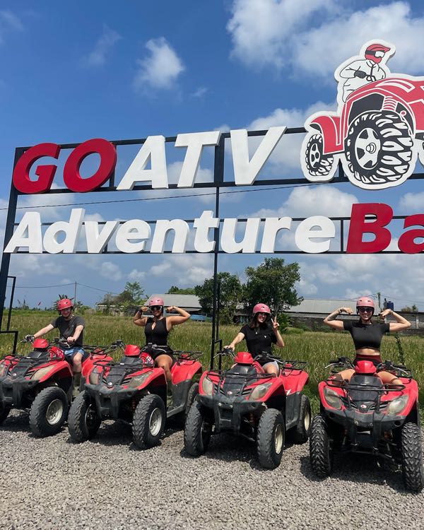 Four riders in helmets on red quad bikes in front of an ATV park sign