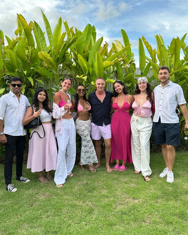 A group of friends dressed up, posing on a lawn in front of tropical plants