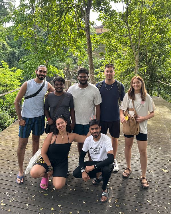 A group of hikers posing on a wooden boardwalk surrounded by tall trees