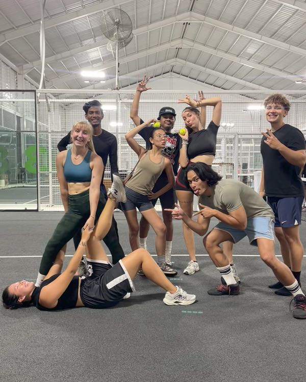 A group striking playful poses on an indoor padel court