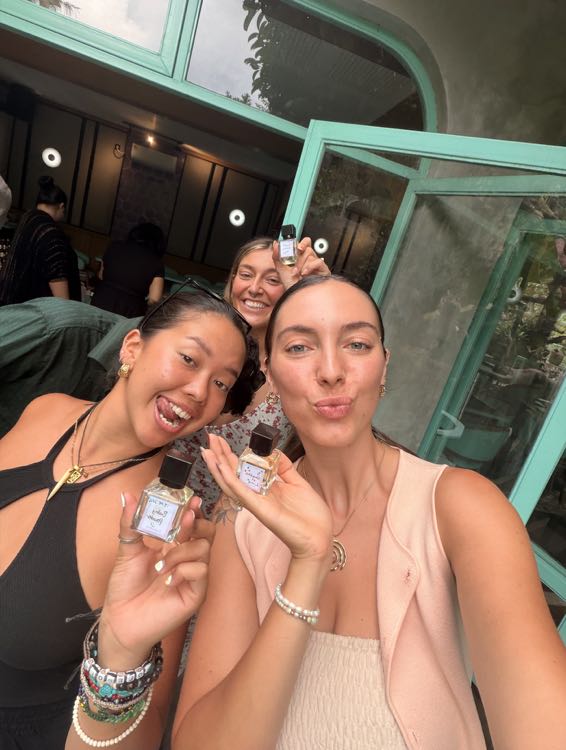 Three smiling friends holding up small perfume bottles they made