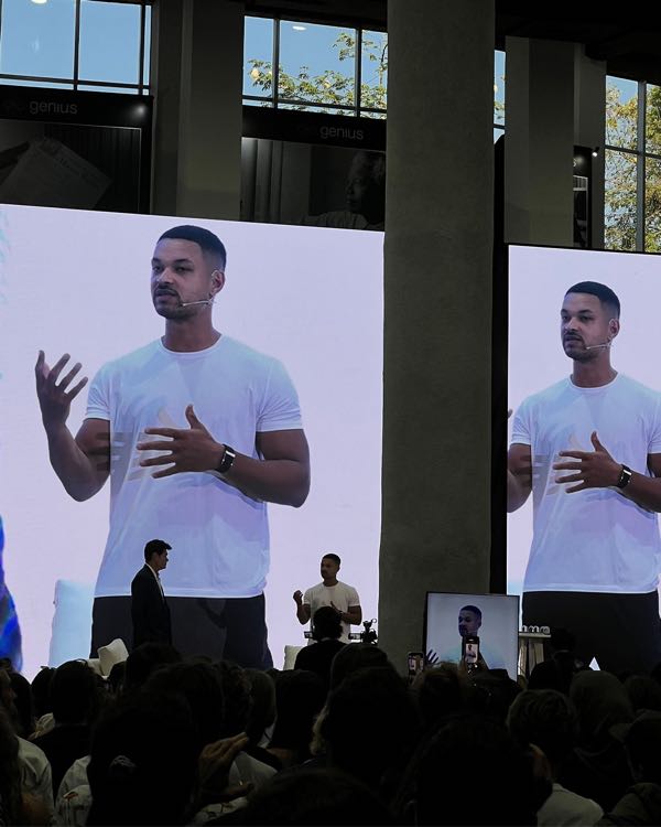 A speaker on stage, shown on two large screens in front of a seated audience