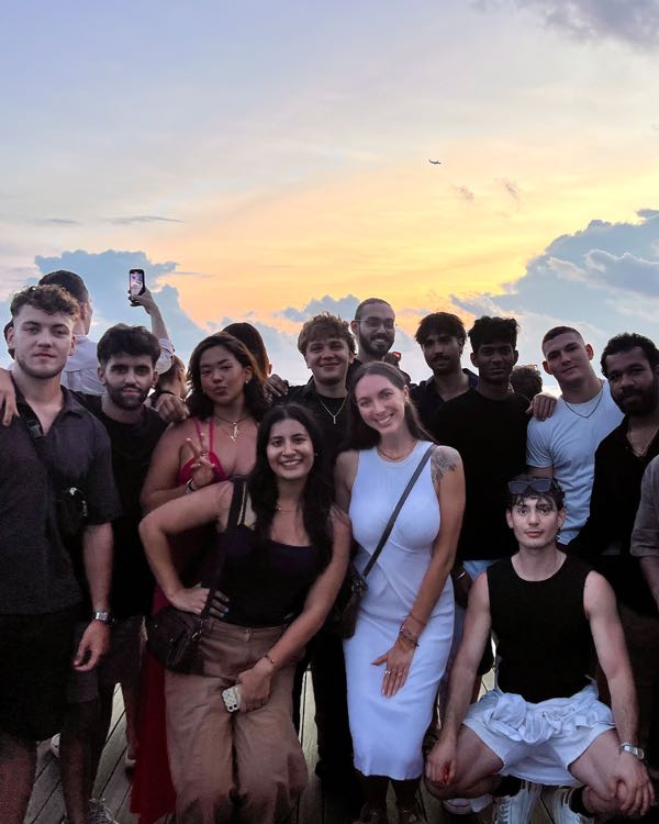 A group of friends posing together under a pink sunset sky
