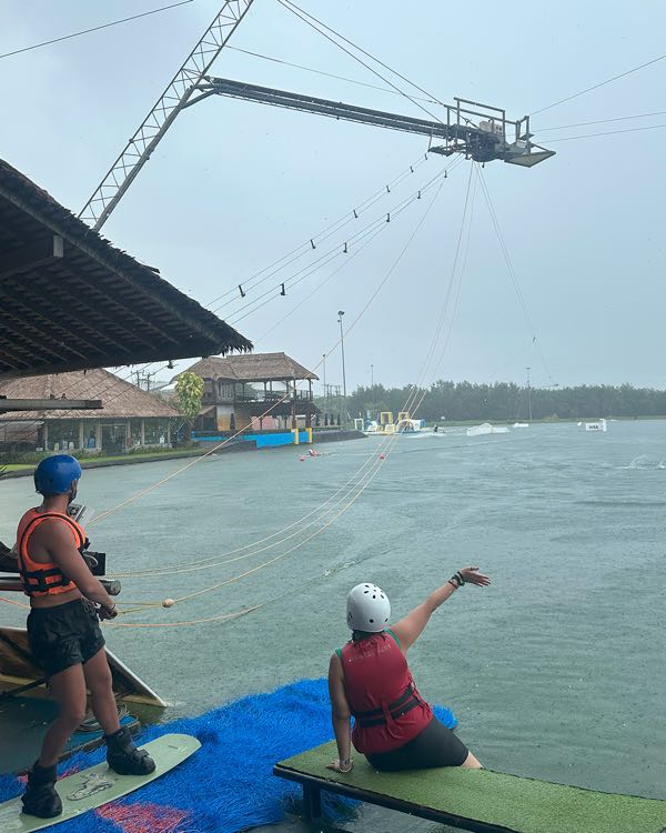 Two people in life jackets on a dock at a wakeboard cable park