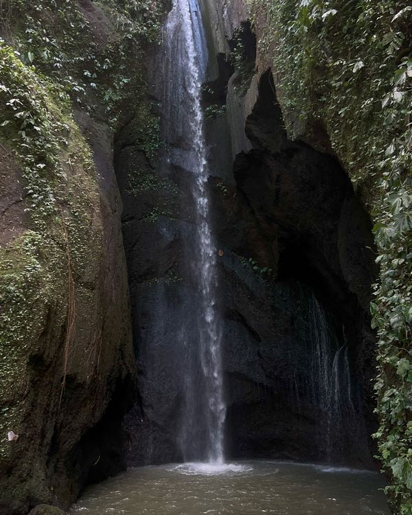 A tall, narrow waterfall falling into a dark, moss-covered gorge