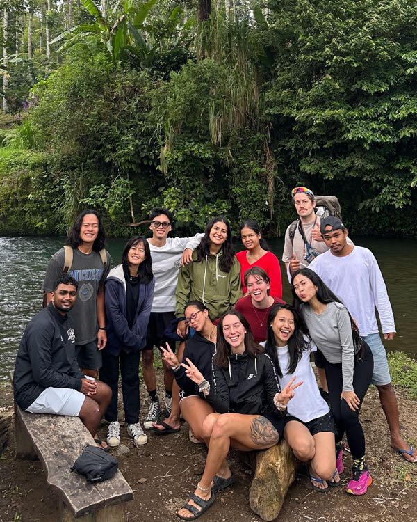 A group of interns posing at a campsite beside a river, with lush green trees around them